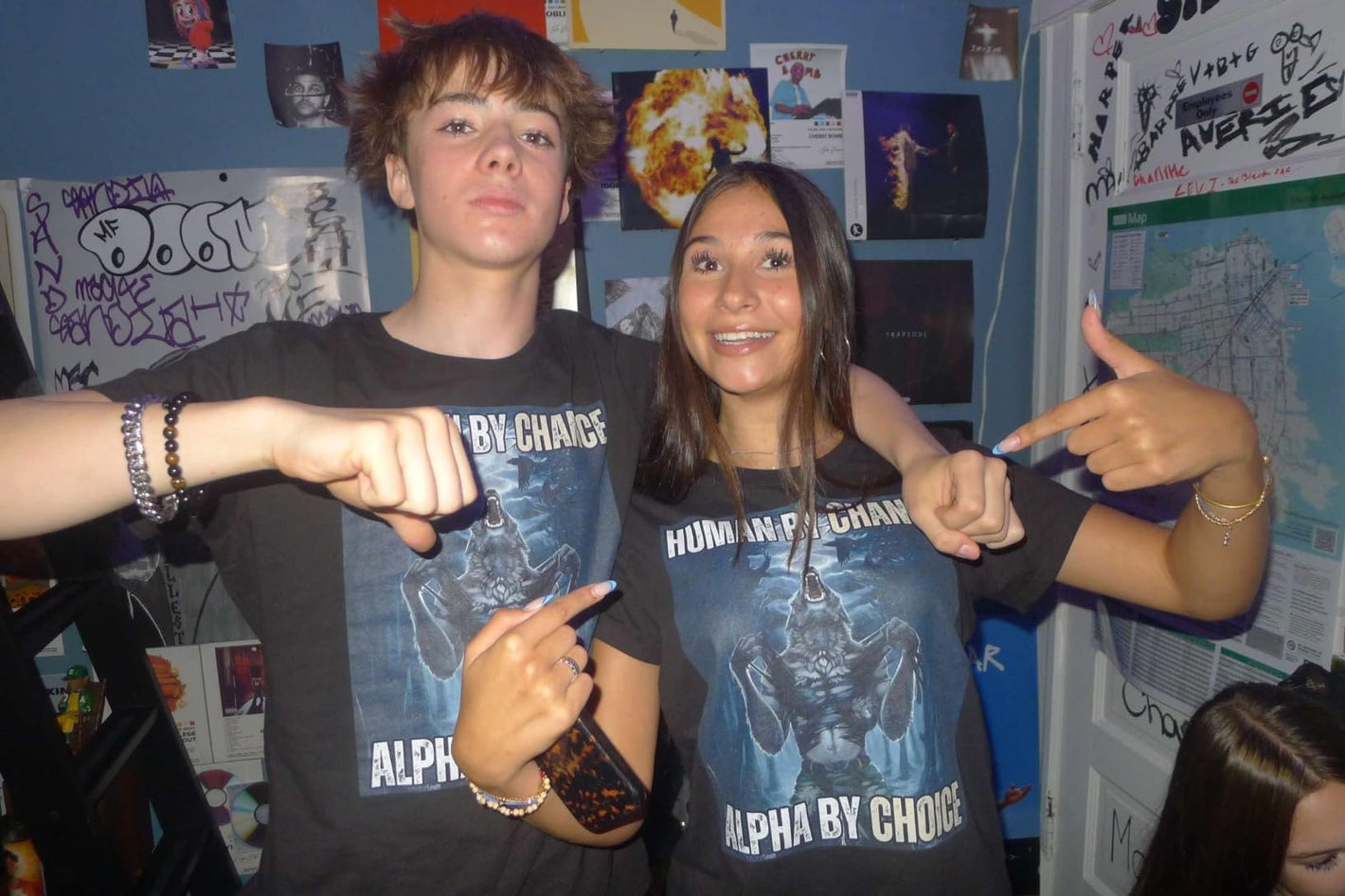 Two people wearing matching t-shirts with text in a room with posters on the wall.
